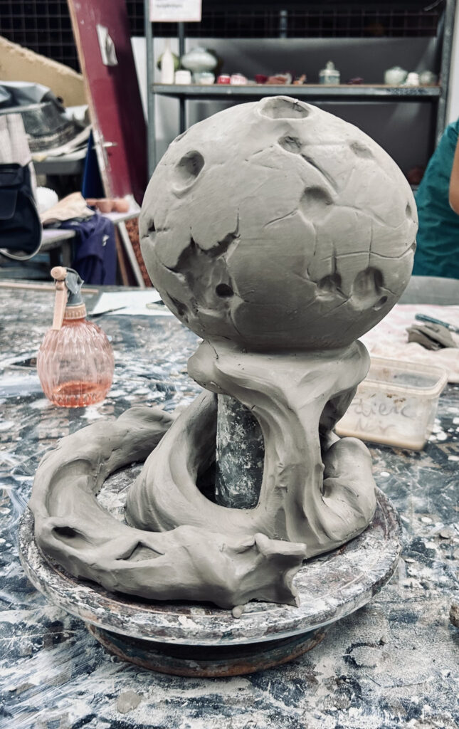 Sculpture en terre avant cuisson, avec émaillage blanc et noir, représentation d'une lune sur un drapé de nuages veloutés